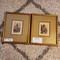 Two framed architectural scene prints in gold frames on carpet