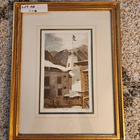Framed collectible print showing a winter scene with a tower, snow-covered buildings, and mountains with an American flag atop the tower. Gold tone frame with cream and green matting.
