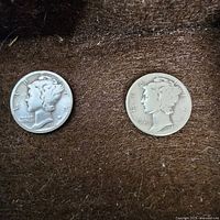 Two silver Mercury dimes dated 1936 and 1940 laid on a brown fabric background.