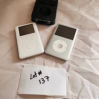 Two vintage Apple iPods and a black leather case placed on a white surface with a Lot #137 card visible.