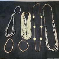 Photo showing all 7 necklaces laid out on black fabric background for full lot overview.