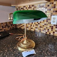 Side view of vintage brass lamp with green shaded dome and pull chain switch on tiled countertop.