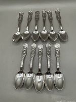 Full view of all 11 commemorative silver plate spoons arranged in two rows showing different relief portraits on handles