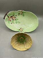 Two Carleton Ware bowls shown together: large leaf-shaped green bowl with apple blossom decoration and smaller yellow buttercup bowl in front.