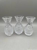 Front view of three clear cut crystal bud vases with textured lower halves and flared rims on gray background