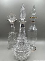 Three cut glass decanters placed side by side showing varying shapes and silver collars.