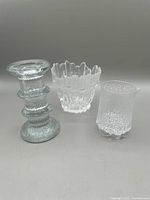 Three clear glass decorative pieces: a textured bubble patterned creamer with spout on the right, a crown-rimmed vase or candle holder center, and a ridged ring shape candlestick on the left.