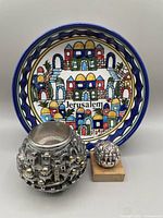 Front display of the sterling globe candle holder, the small sterling sculpture on stone base, and Jerusalem ceramic bowl together showing cityscape designs and colors.