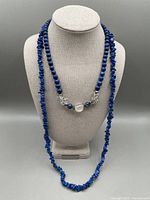 Two lapis lazuli necklaces displayed on a grey fabric bust. One necklace is made of polished deep blue lapis chip beads approximately 34 inches in length. The other necklace is shorter at 18 inches, composed of round lapis beads combined with rock crystal beads.