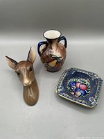 Doe head wall plaque, Tunstall vase, and ashtray arranged on a gray surface