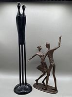 View of both sculptures together showing the elongated couple sculpture and the dancing couple sculpture side by side on a white background