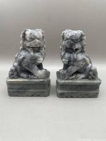 Front-facing photo of both carved greenstone Foo dogs showing their full bodies on bases.