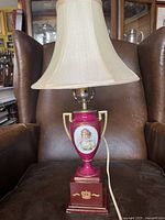 Full view of porcelain urn lamp with wooden base and cream fabric shade.