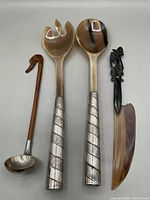 Photo of seven salad servers with metal handles and natural material heads, ladle with wooden handle and metal bowl, letter opener with natural blade and dark handle.