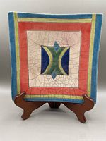 Front view of square raku pottery platter with multi-color geometric design and visible raku crackle glaze.