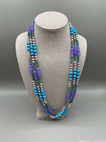 Full view of the multi-strand necklace displayed on a necklace bust, showing the arrangement of blue, violet, and pearl-like beads.