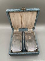 Boxed grooming set showing two brushes and one comb inside a blue textured box with satin lining.