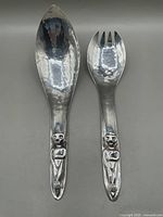 Pair of hand hammered silver-plated salad servers with Kwakiutl design figures on handles, spoon and fork shown top view.