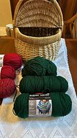 Wicker picnic basket upright open with skeins of green and red yarn stacked in front and inside
