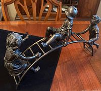 Side view showing three children playing on arched jungle gym playground apparatus. Sculpture appears to be made from cast metal with a bronze finish.