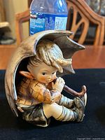 Front side view of the Umbrella Boy figurine showing the boy holding an umbrella, sitting.