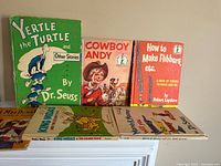 Photo of six vintage children’s books showing front covers including 'Yertle the Turtle and Other Stories' by Dr. Seuss in green, 'Cowboy Andy', 'How to Make Flibbers etc.' and four Dr. Seuss books with white spines on shelf.