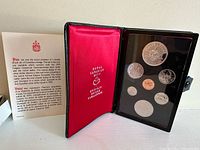 Full view of coin set inside the black display case with red satin lining, showing all coins and documentation insert alongside.