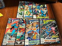 Lot of 7 Superman comic books laid out on wooden surface with a water bottle visible, showing all comics' front covers.