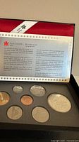 The seven commemorative coins arranged in the original foam display case, with informational leaflet displayed.