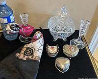Front view of all items on black surface with water bottle for scale, showing Mikasa candlestick holders, Star of David candy bowl with lid, ladies scarf rolled and vintage trinket boxes.