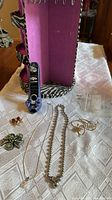 Pink and purple jewelry organizer with zebra print trim visible, assorted vintage jewelry items laid out on table including necklaces, brooches, earrings, and rings