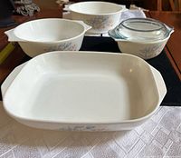 All five pieces of the Blue Iris milk glass bakeware set arranged with the rectangular dish in front and the three round casseroles behind, one with lid.