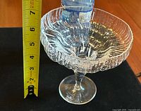 Clear textured glass footed compote with measuring tape showing height about 6.6 inches.
