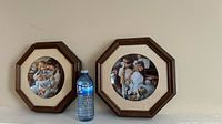 Photo of the front of the two framed collector plates alongside a water bottle to show scale. The plates show artwork of children in vintage style wooden octagonal frames with fabric matting.