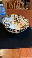 Top and interior view of octagonal bowl showing detailed Imari floral design in black, white, red and gold accents, alongside a water bottle for scale.