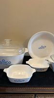 Seven-piece vintage Corningware Blue Cornflower set: large casserole with lid, two petite casserole dishes, pie plate showing Blue Cornflower pattern