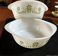 Two milk glass casserole dishes with green floral Primrose Dream pattern, stacked to show handles and pattern details