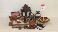 Photo of assorted animal-themed carved wood figures, metal picture frame, woven bowl, painted pottery, decorative box, and harmonica.