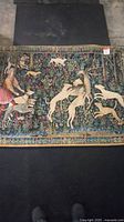 Full view of the tapestry showing the overall medieval hunting scene with hunter, dogs and stag.