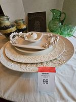Overall view of stack of cream-colored ceramic platters, candle holder, basket dish, and green glass pitcher and glasses on table