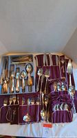 Top view of silverware sets arranged in trays and purple cloth holders showing forks, spoons, and knives from both Reed and Barton and Holmes and Edwards Deepsilver.