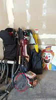 Overview of tennis and golf equipment leaning against wall alongside cornhole board and bike rack