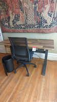 Assembled Vari standing desk and black mesh office chair in front of wall tapestry on hardwood floor