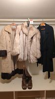 All items displayed together hung on rack: two fur coats, cashmere coat, and boots
