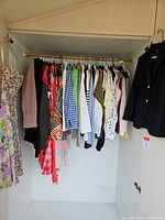 Full view of assorted hanging garments in closet, including dresses, tops, skirts and blazers