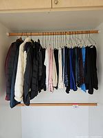 Clothes hanging on wooden rod including multiple jackets and various tops or jeans on hangers