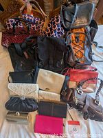 Full view of the collection of handbags, purses, wallets, and backpacks laid out on a bed, showing various sizes, colors, and styles.