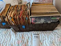 Photo showing a basket filled with numerous 45 RPM vinyl records in paper sleeves, arranged vertically and horizontally.