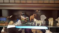 Shelf showing multiple animal figurines including a wood duck, bear, seals, polar bear, ram, and fish figurines