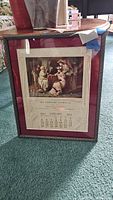 Front view of the framed 1913 calendar with vintage image of three women and company name printed below.